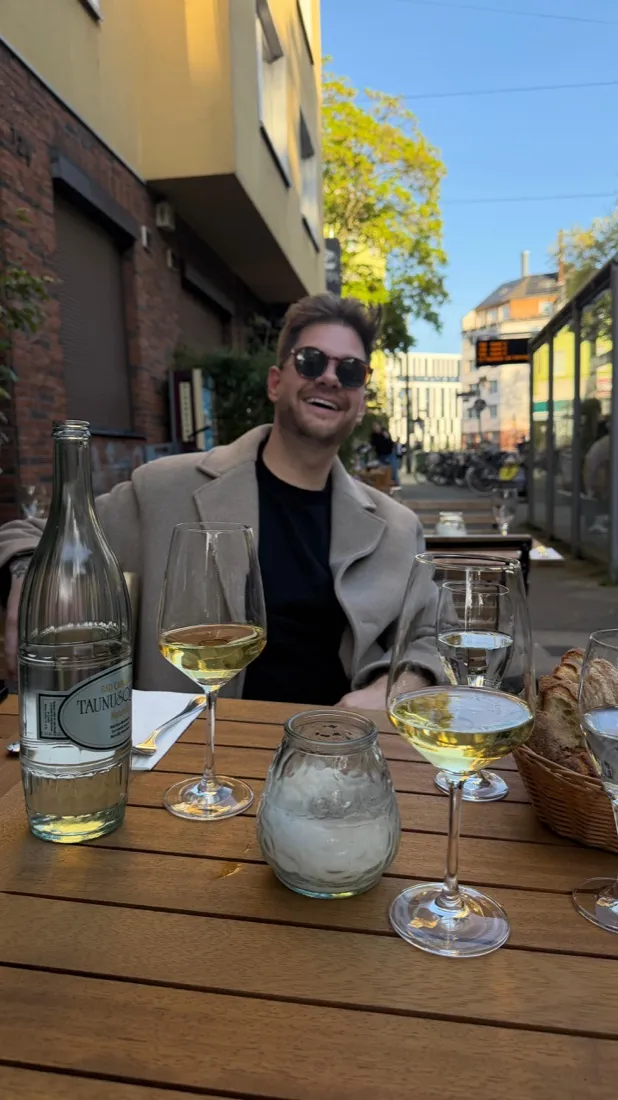 Julian mit Weißwein an einem Tisch draußen